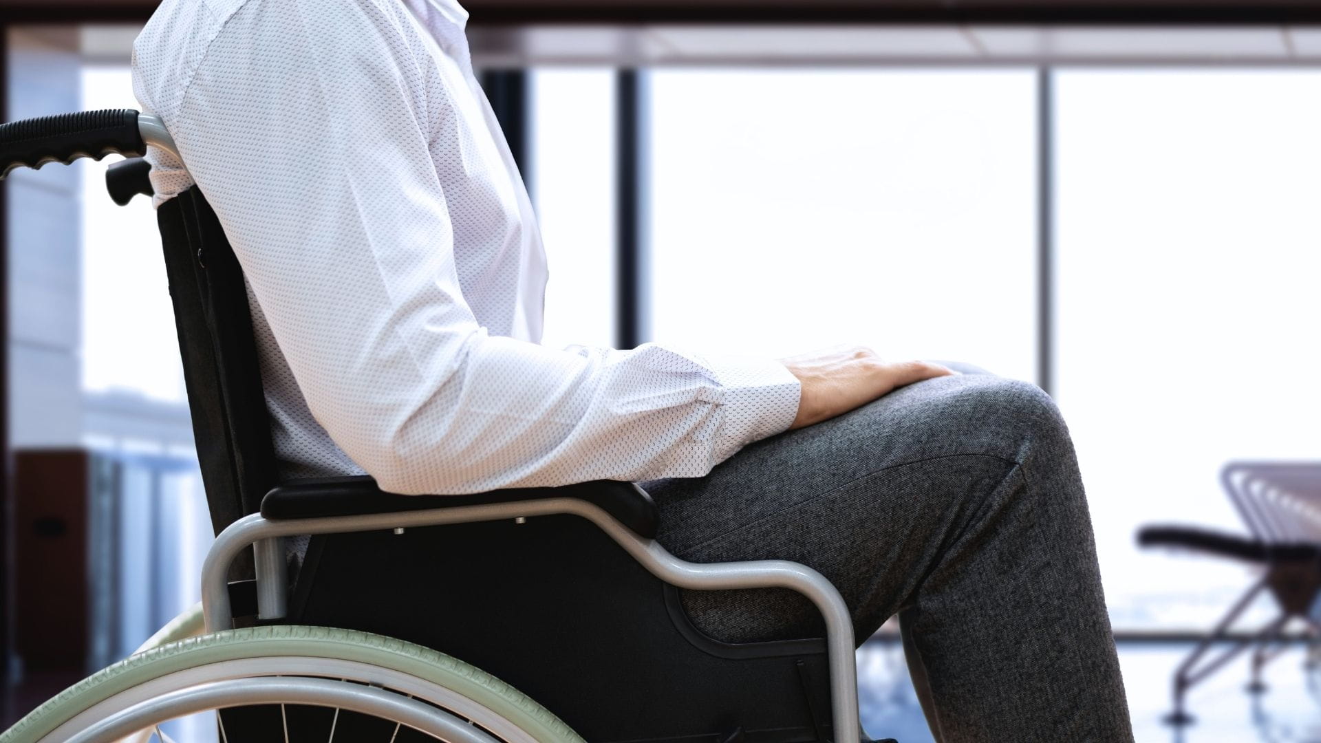 Passenger with reduced mobility seated in a wheelchair inside a modern airport terminal for dedicated airport assistance.